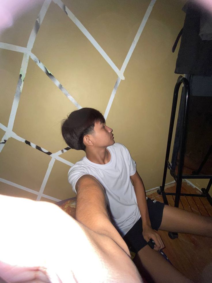 a young man sitting on the floor in front of a wall with tape taped to it