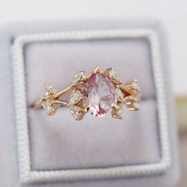 a pink diamond ring sitting on top of a velvet box