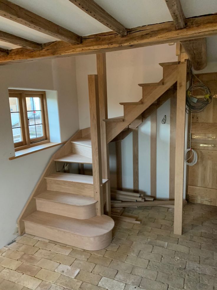 an empty room with wooden stairs and tile flooring in front of a window on the far wall