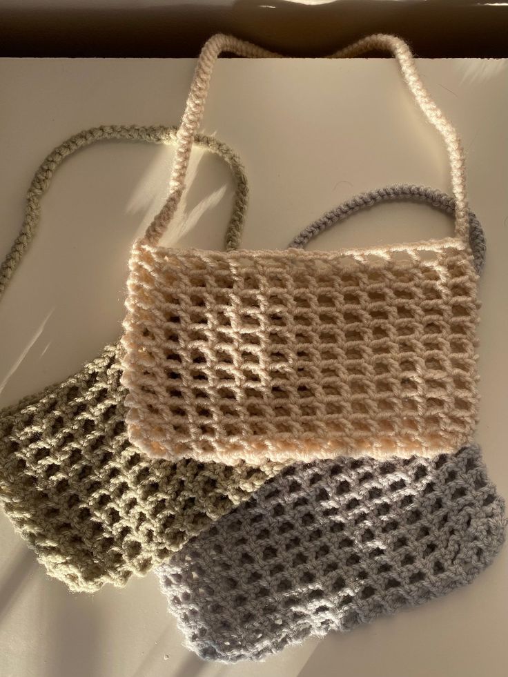 three crocheted purses sitting on top of a white table next to each other