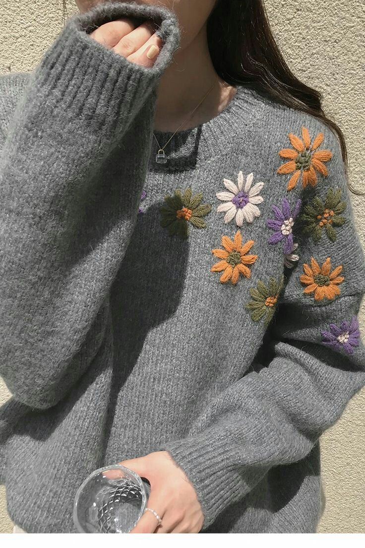 a woman wearing a gray sweater with flowers on it and holding her hand up to her face