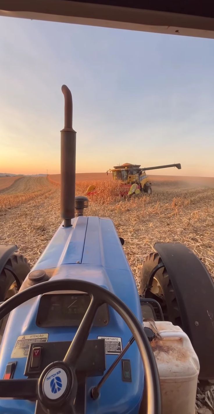 a blue tractor driving down a dirt road next to a large tank in the middle of a field