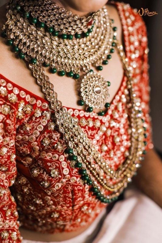 a woman wearing a red and gold sari with green beads on her neck, in front of a white background