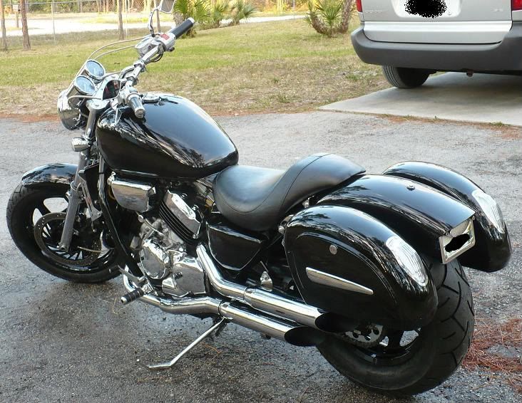 a black motorcycle parked in a parking lot next to a white van and some grass