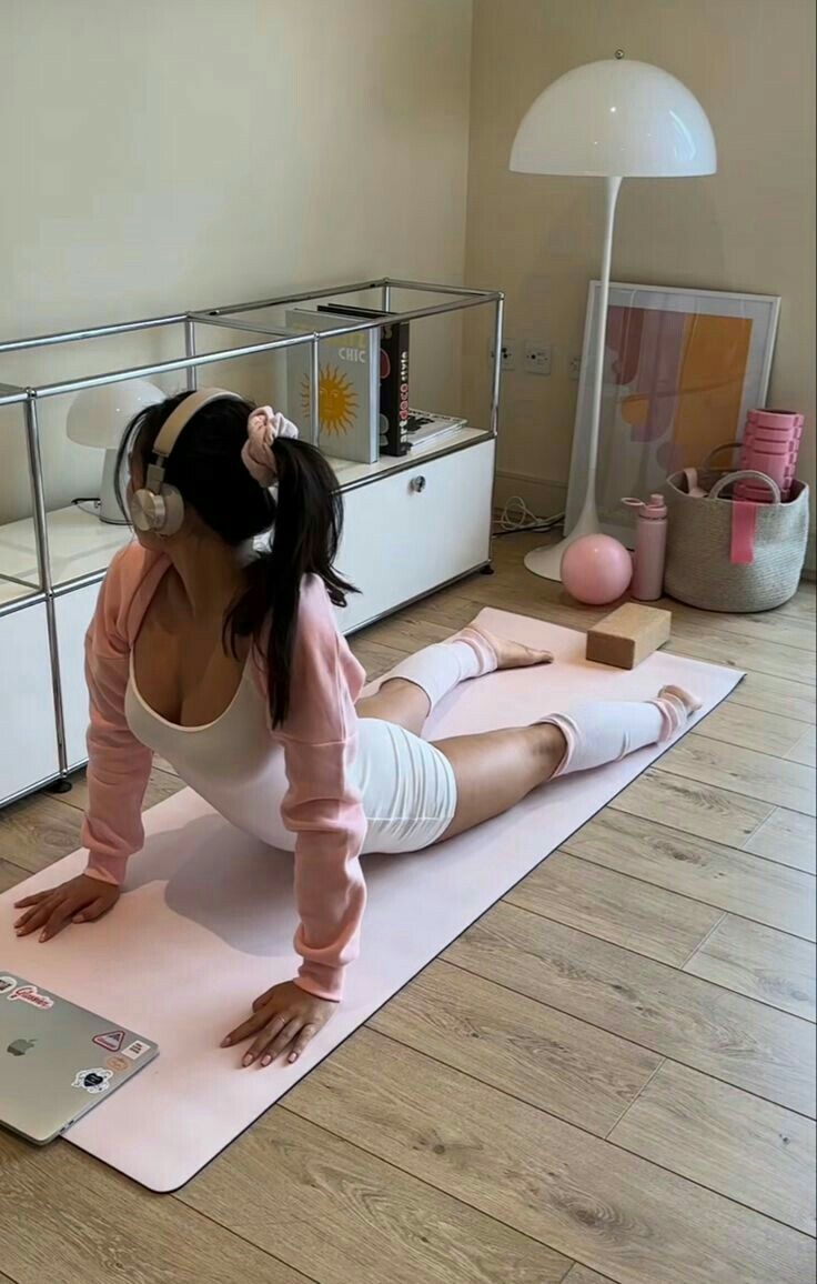 a woman sitting on top of a yoga mat with headphones in her ears while using a laptop computer