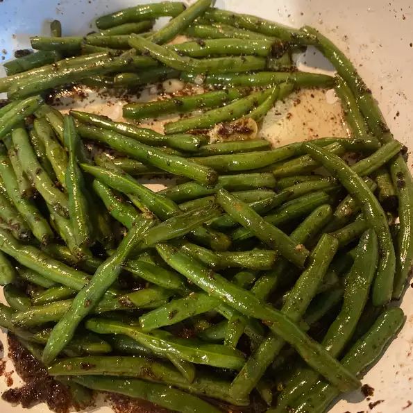 green beans are being cooked in a white bowl with seasoning sprinkles