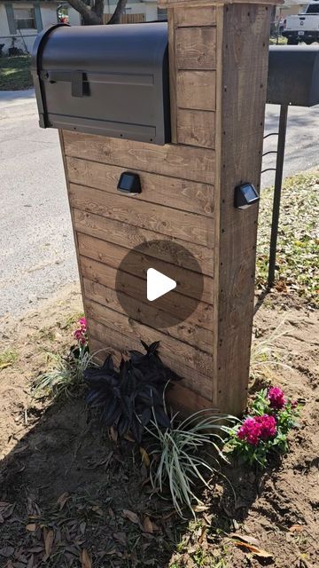 a wooden mailbox sitting on the side of a road next to a flower bed