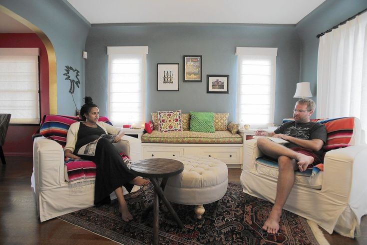 two people sitting on couches in a living room with blue walls and white curtains