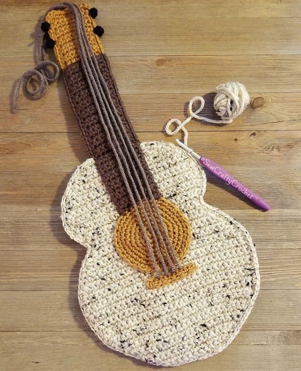 a crocheted guitar sits on a wooden floor next to yarn and knitting needles