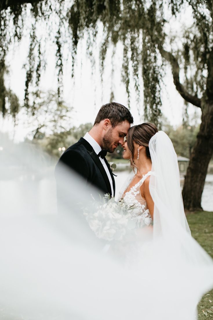 a bride and groom standing under the trees