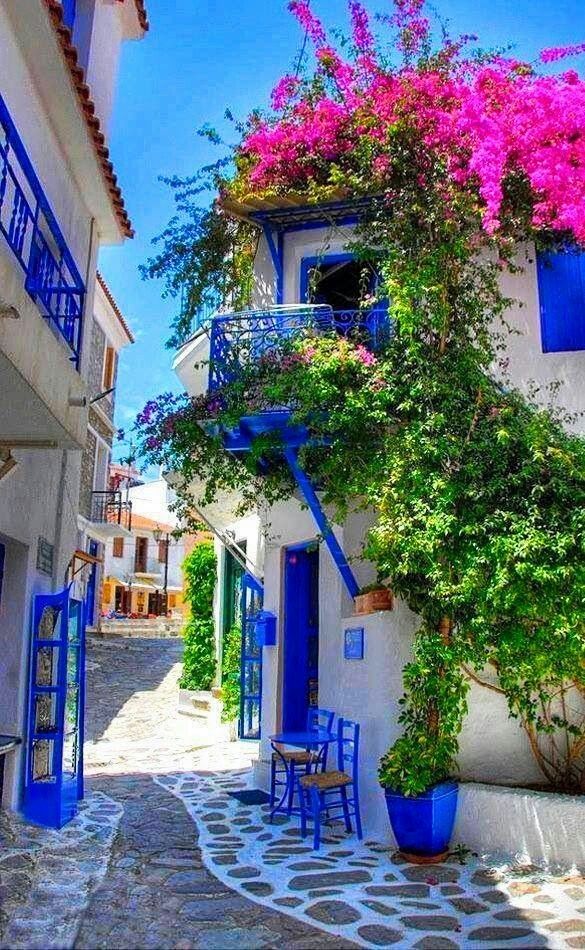 an alleyway with blue doors and flowers growing on the side of it, surrounded by white buildings