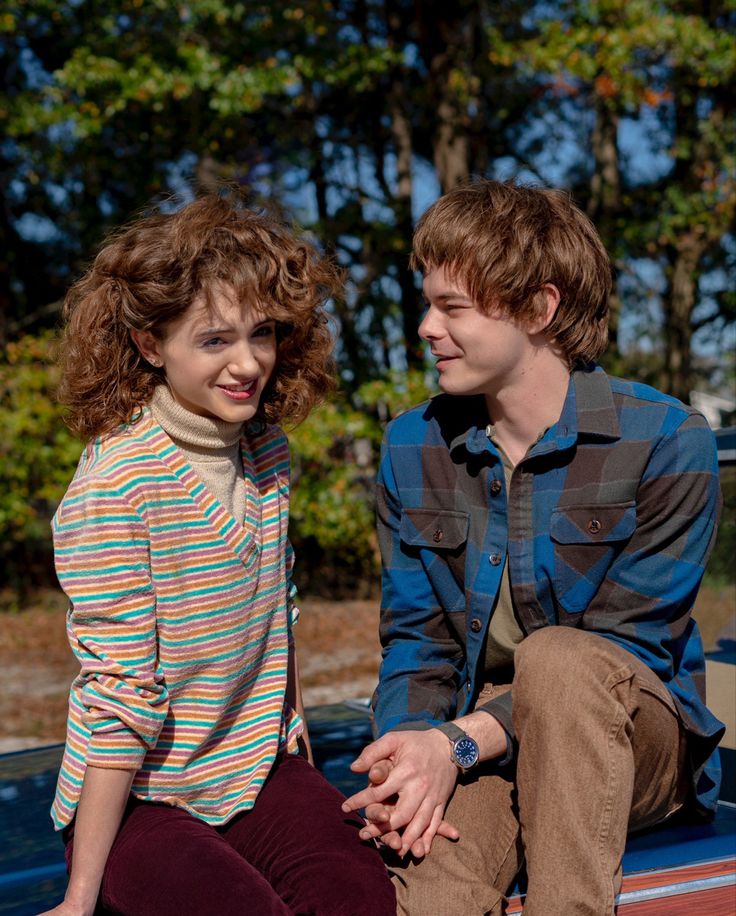 two people sitting on the back of a pick up truck in front of some trees