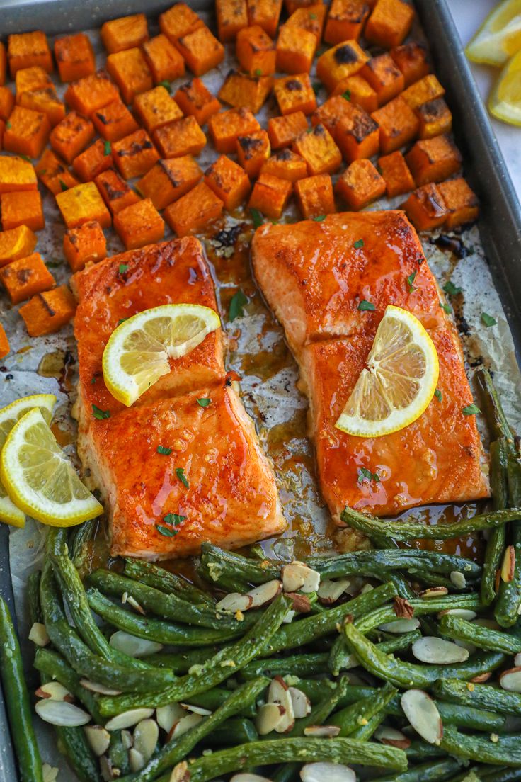 salmon, green beans and sweet potatoes on a baking sheet with lemon wedges for garnish