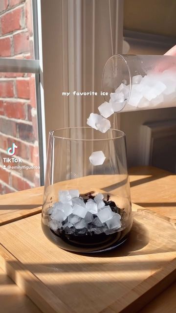 someone pouring ice into a wine glass on top of a wooden table next to a window