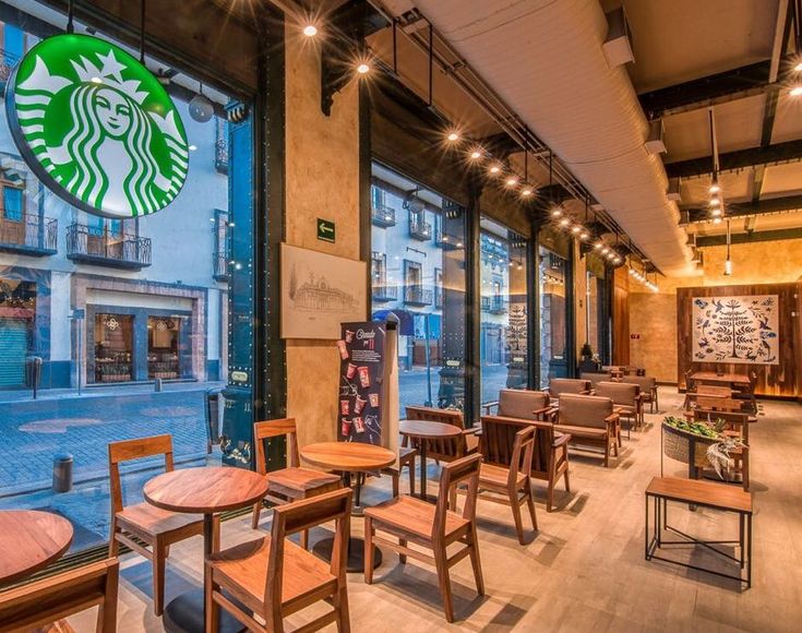 the interior of a starbucks coffee shop with tables and chairs in front of large windows