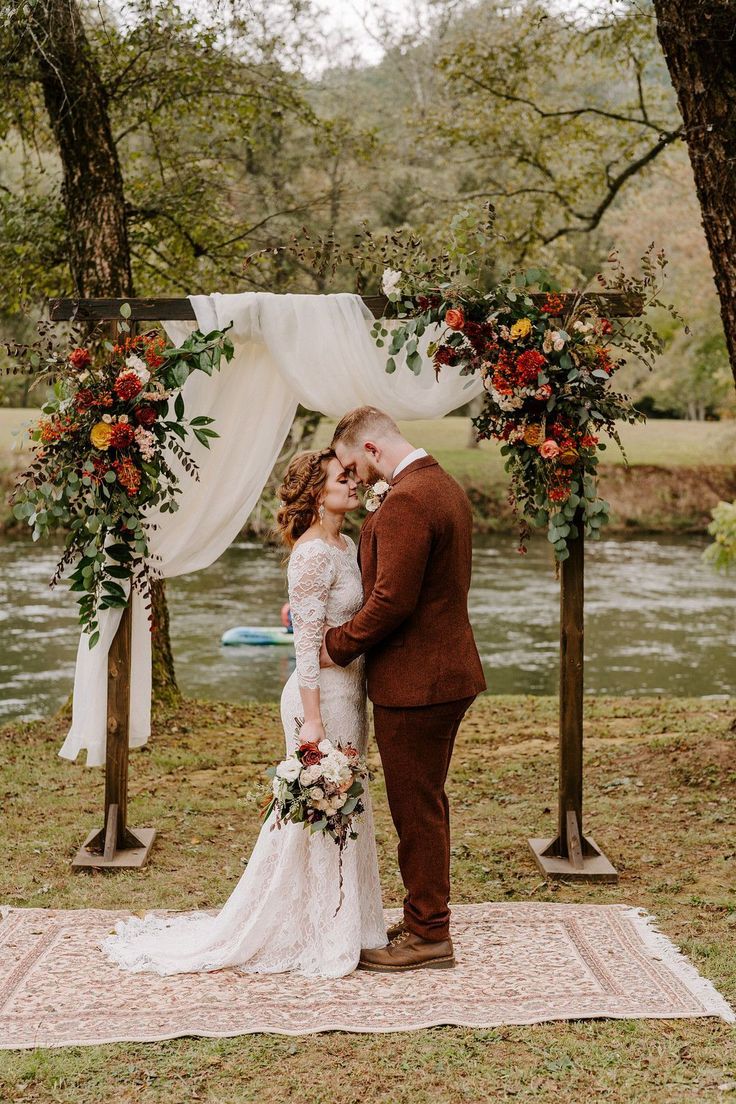 a bride and groom standing under an arch with flowers on it in front of a river