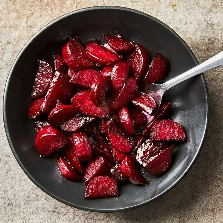 a bowl filled with sliced beets on top of a stone counter next to a spoon