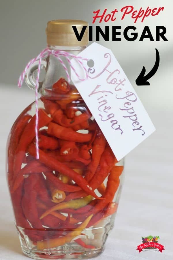 a bottle filled with hot peppers sitting on top of a table next to a sign that says hot pepper vinegar