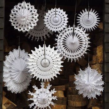 white paper snowflakes hanging from chains in front of firewood stacked on top of each other