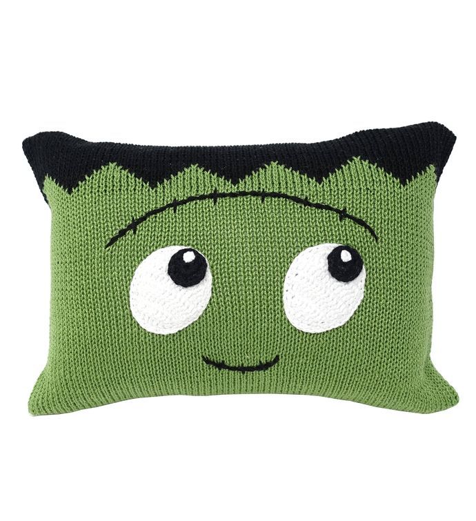 a green knitted pillow with eyes on it