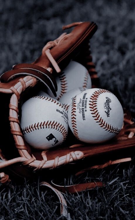 three baseballs are in a catchers mitt on the grass and one is white