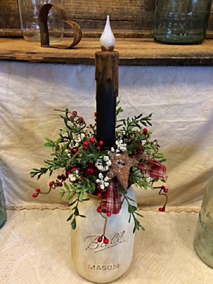 a candle is sitting in a jar with flowers and greenery on it next to other glass jars