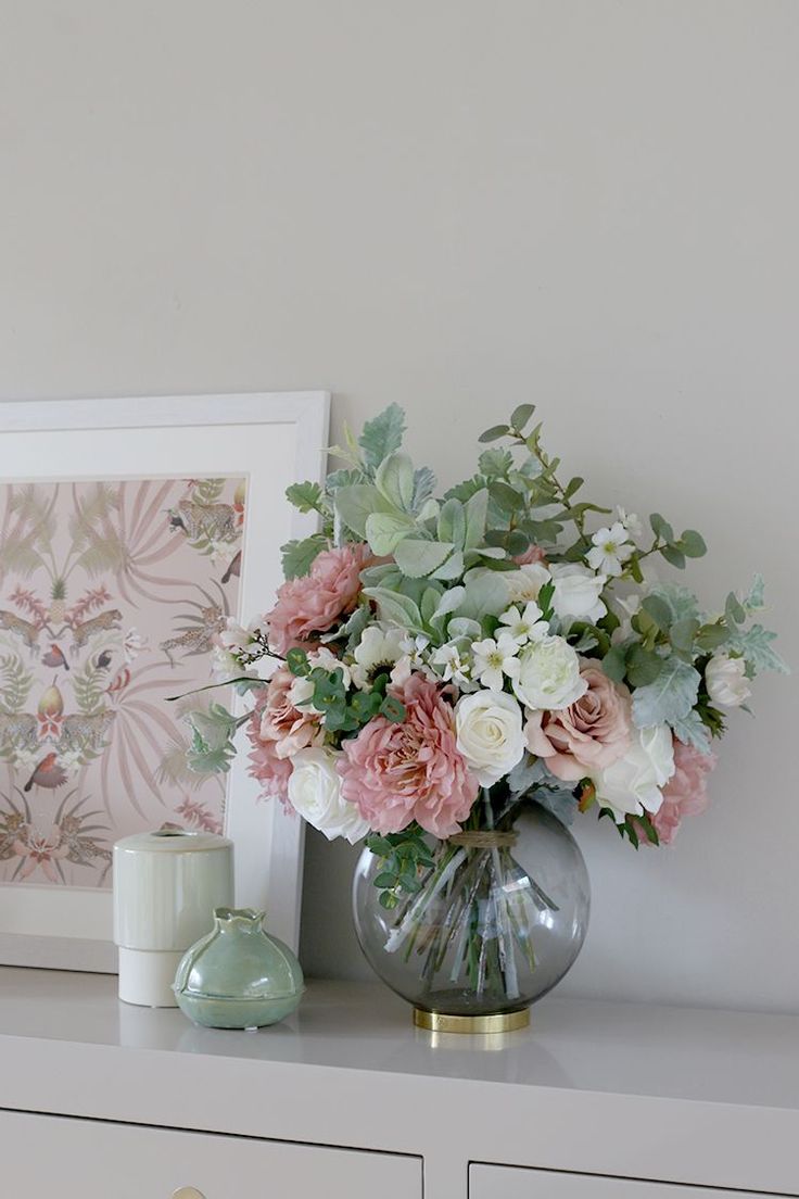 a vase filled with flowers sitting on top of a white dresser next to a candle