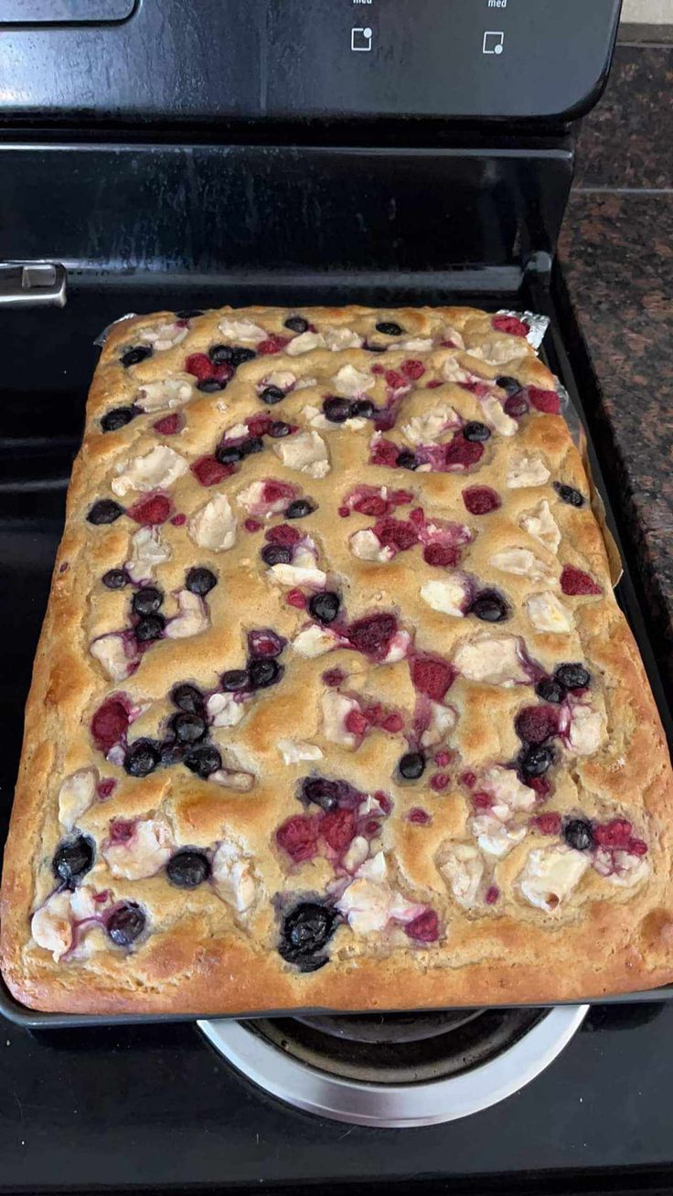 a cake that is sitting on top of a stove with blueberries and raspberries in it