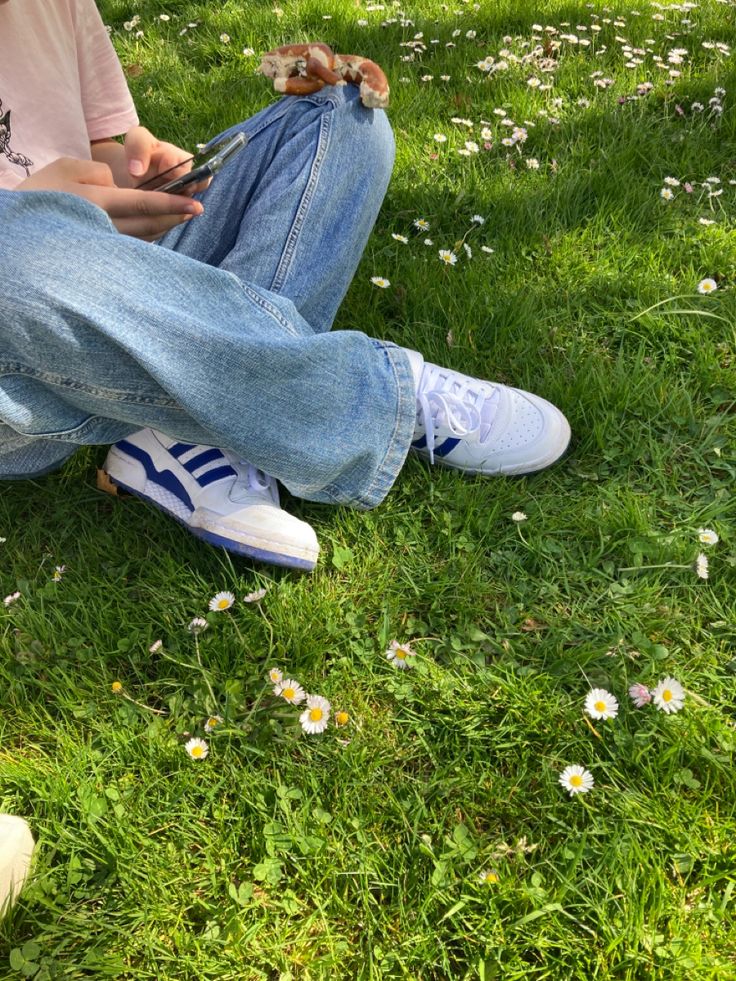 a person sitting on the grass with their cell phone in their hand and looking at them