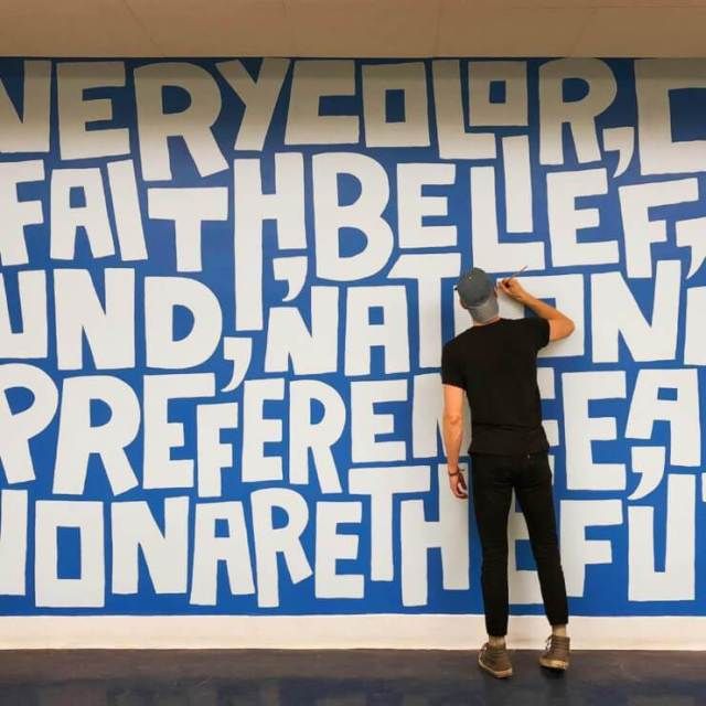 a man standing in front of a blue and white wall with words written on it