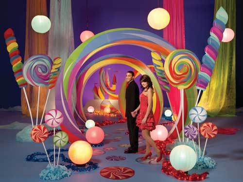 a man and woman standing in front of an assortment of candy land lollipops