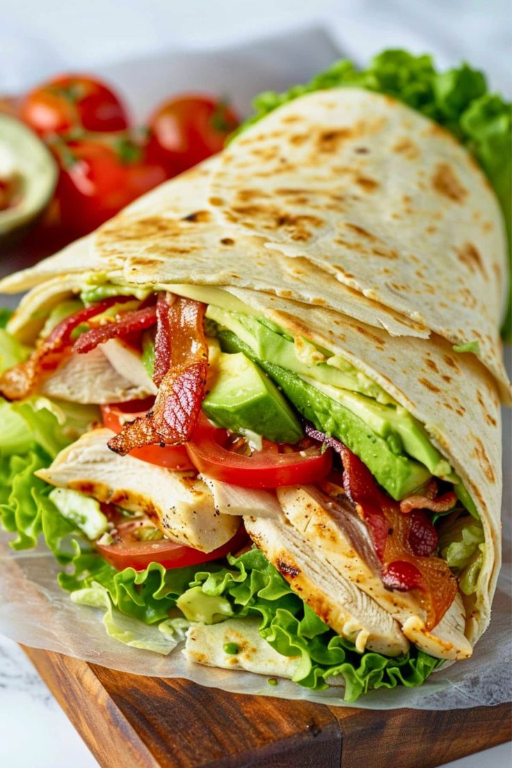 a tortilla with chicken, lettuce and tomatoes on it sitting on a cutting board