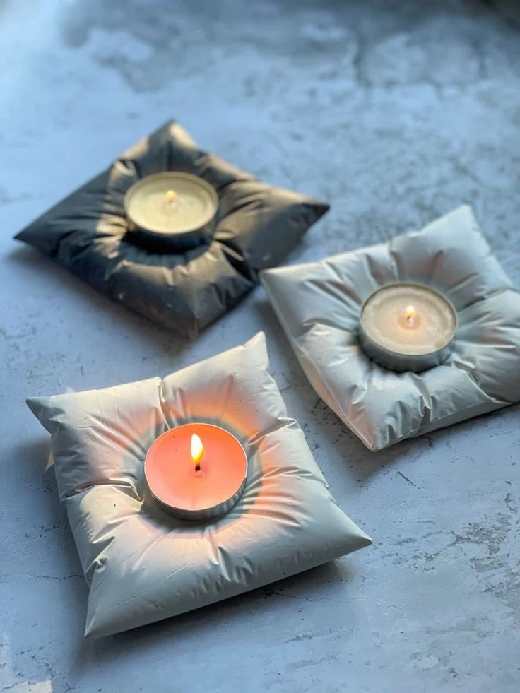 three square pillows with candles in them sitting on a table next to a candle holder