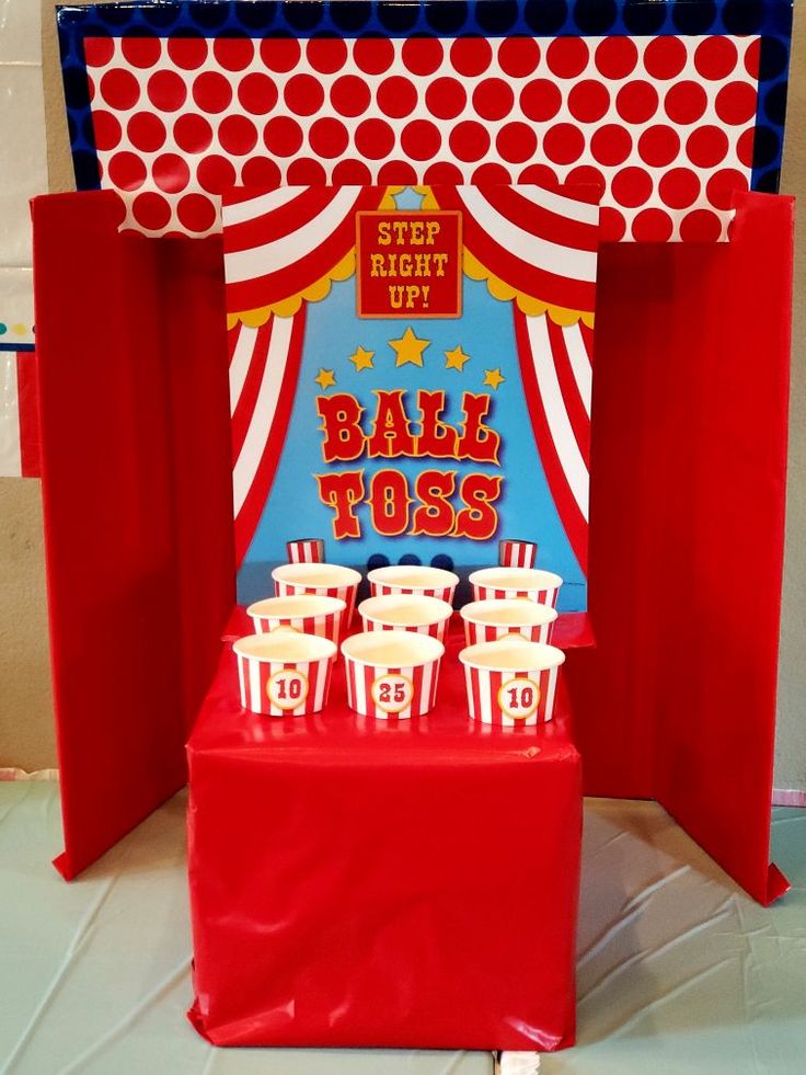 a red table topped with popcorn buckets next to a carnival booth sign that says ball toss