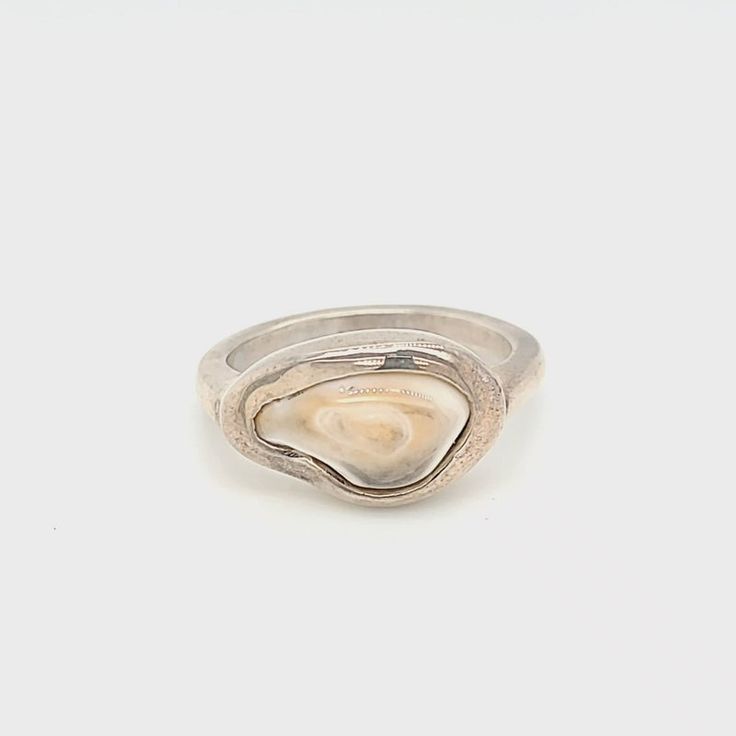 a silver ring with an oyster shell on the front and side, set against a white background