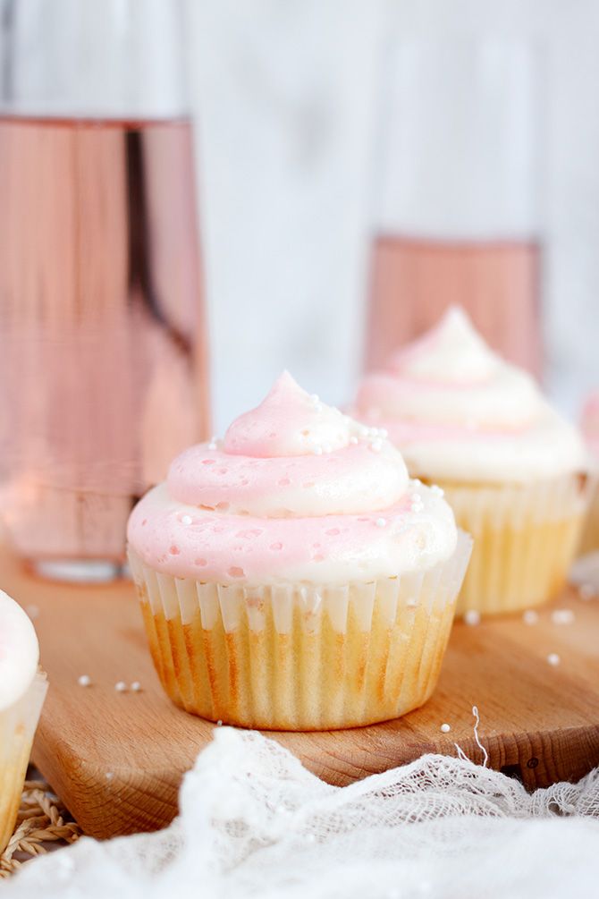 three cupcakes with pink frosting sitting on a wooden board