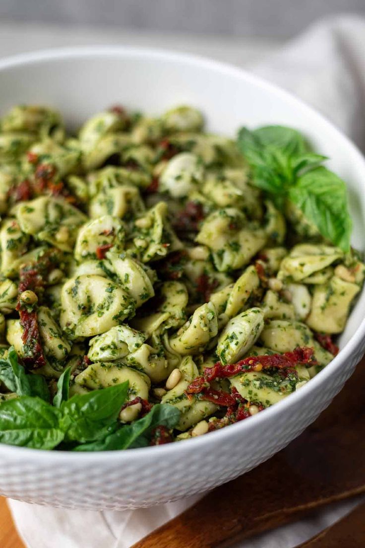 a white bowl filled with pesto pasta on top of a wooden cutting board