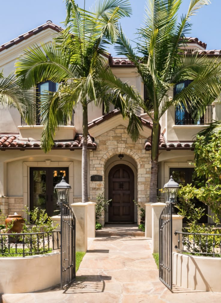 a house with palm trees in front of it and a gated driveway leading to the entrance