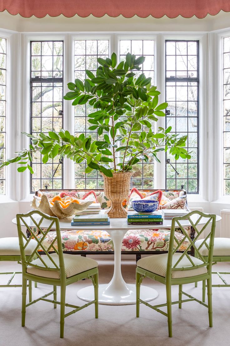 a dining room table with chairs and a potted plant in the center surrounded by windows