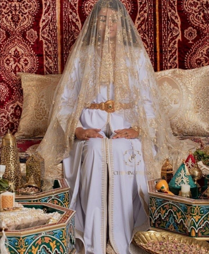 a woman in a white wedding dress and veil standing next to a table with gold decorations on it