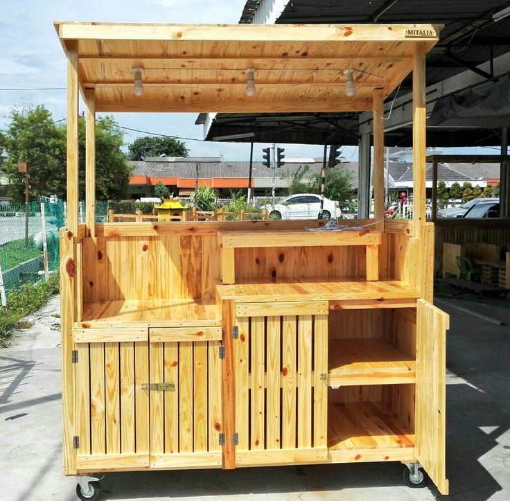 an outdoor wooden stand with shelves and cupboards on it's sides, in front of a parking lot