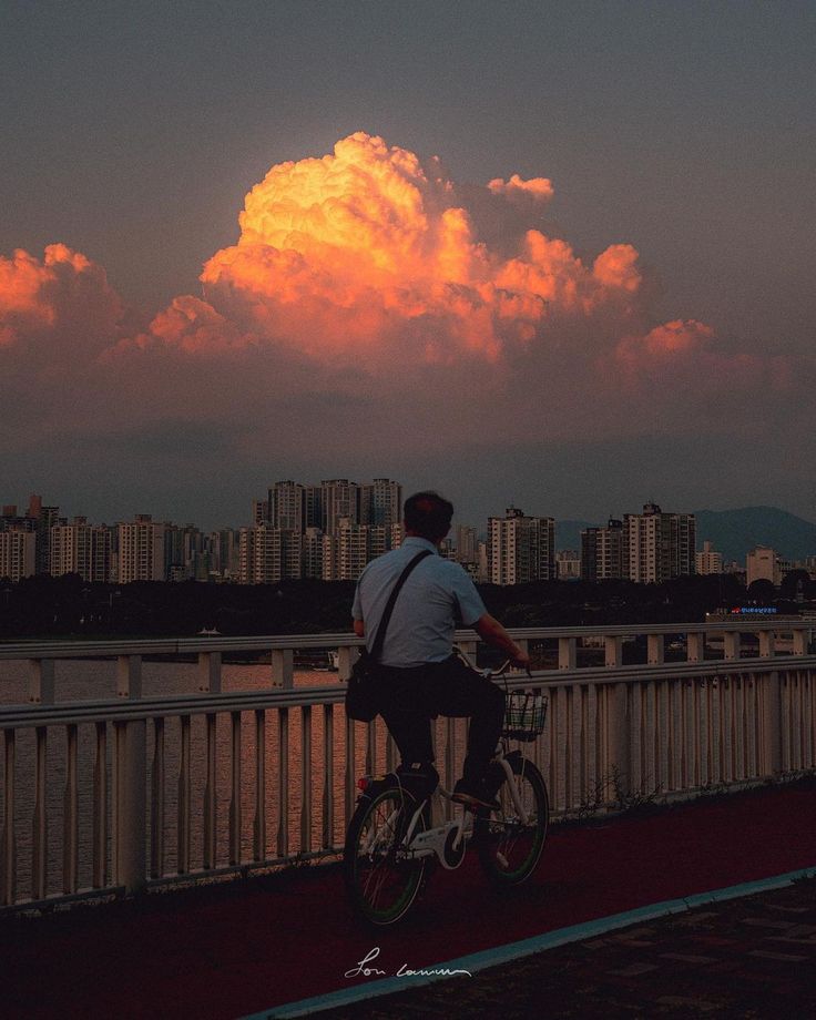 a man is riding his bike on the bridge with clouds in the sky behind him