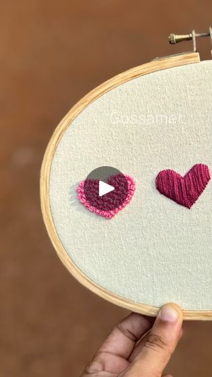 someone is holding up a piece of embroidery with two hearts on it and the other one has a video playing button