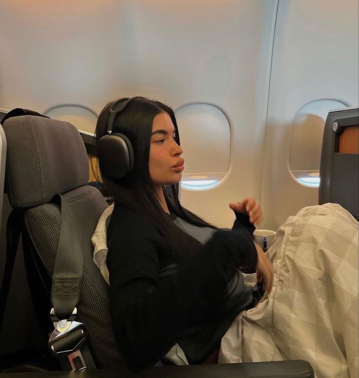 a woman sitting in an airplane with headphones on her ears and holding a cat