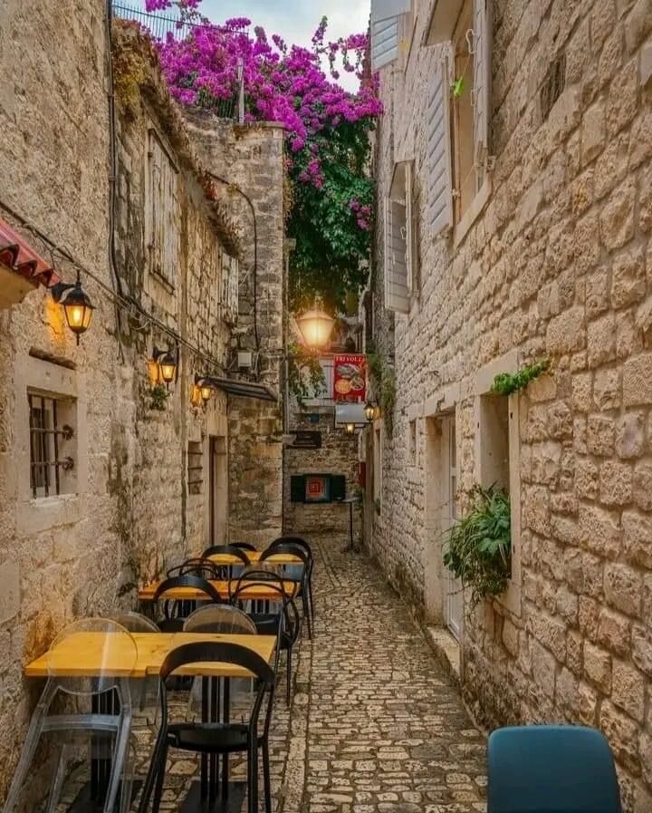 an alley way with tables and chairs lined up along the side walk in front of stone buildings