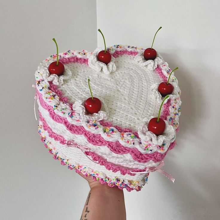 a heart shaped cake with cherries and sprinkles is held by a hand