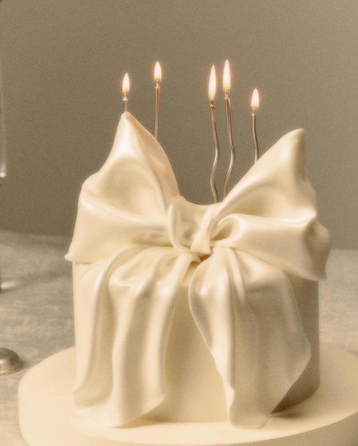 a white cake with candles in the middle and a bow on top that is sitting on a table