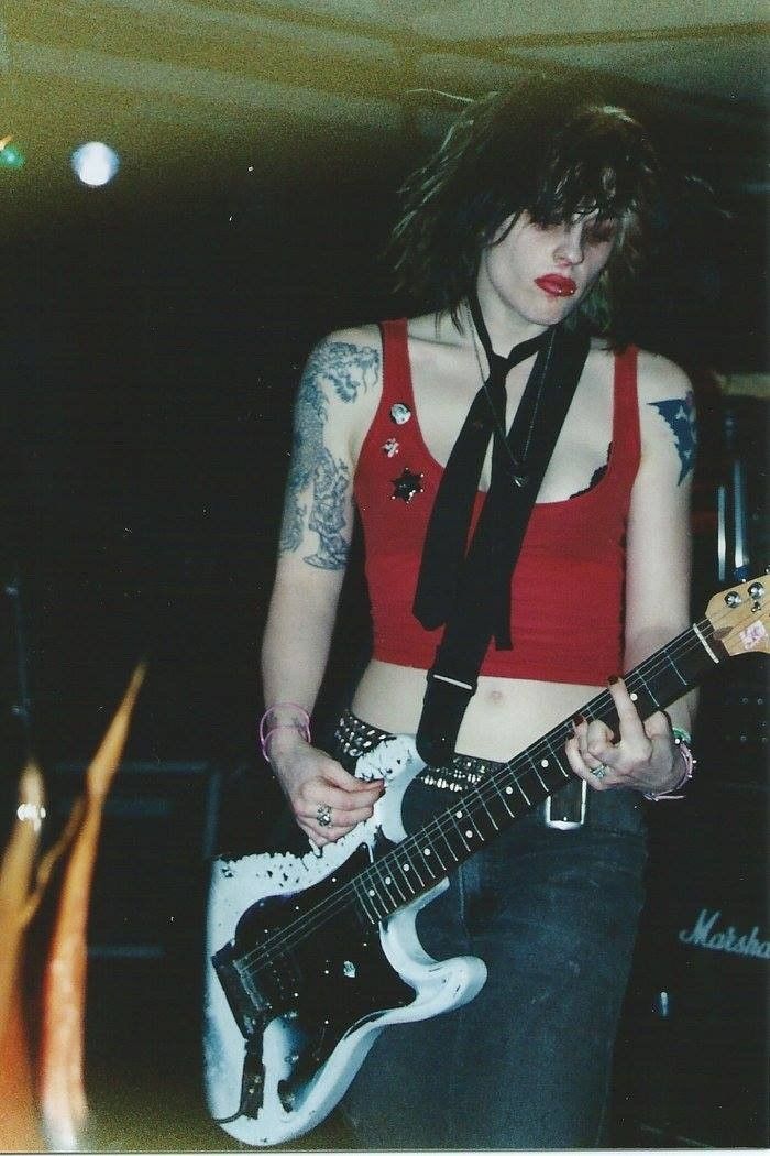 a woman in red shirt and black tie playing an electric guitar with necktie on