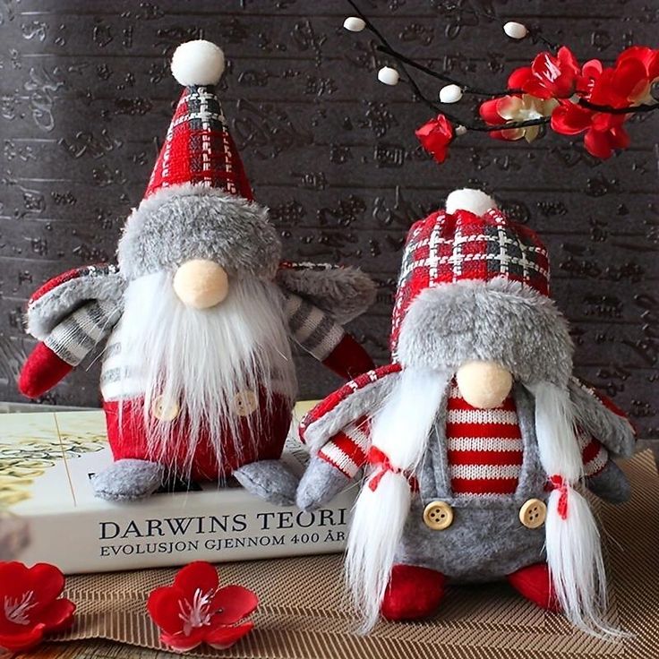 two gnomes sitting on top of a book next to each other with red flowers in the background