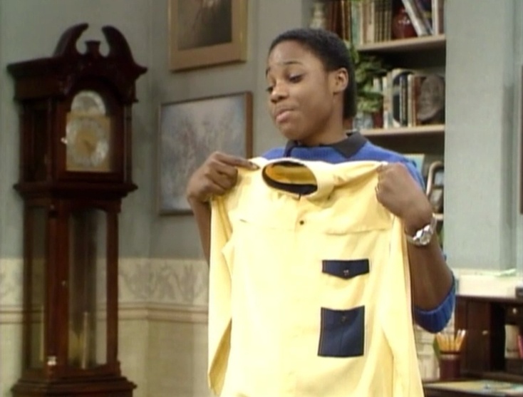 a woman holding up a yellow shirt in front of a clock